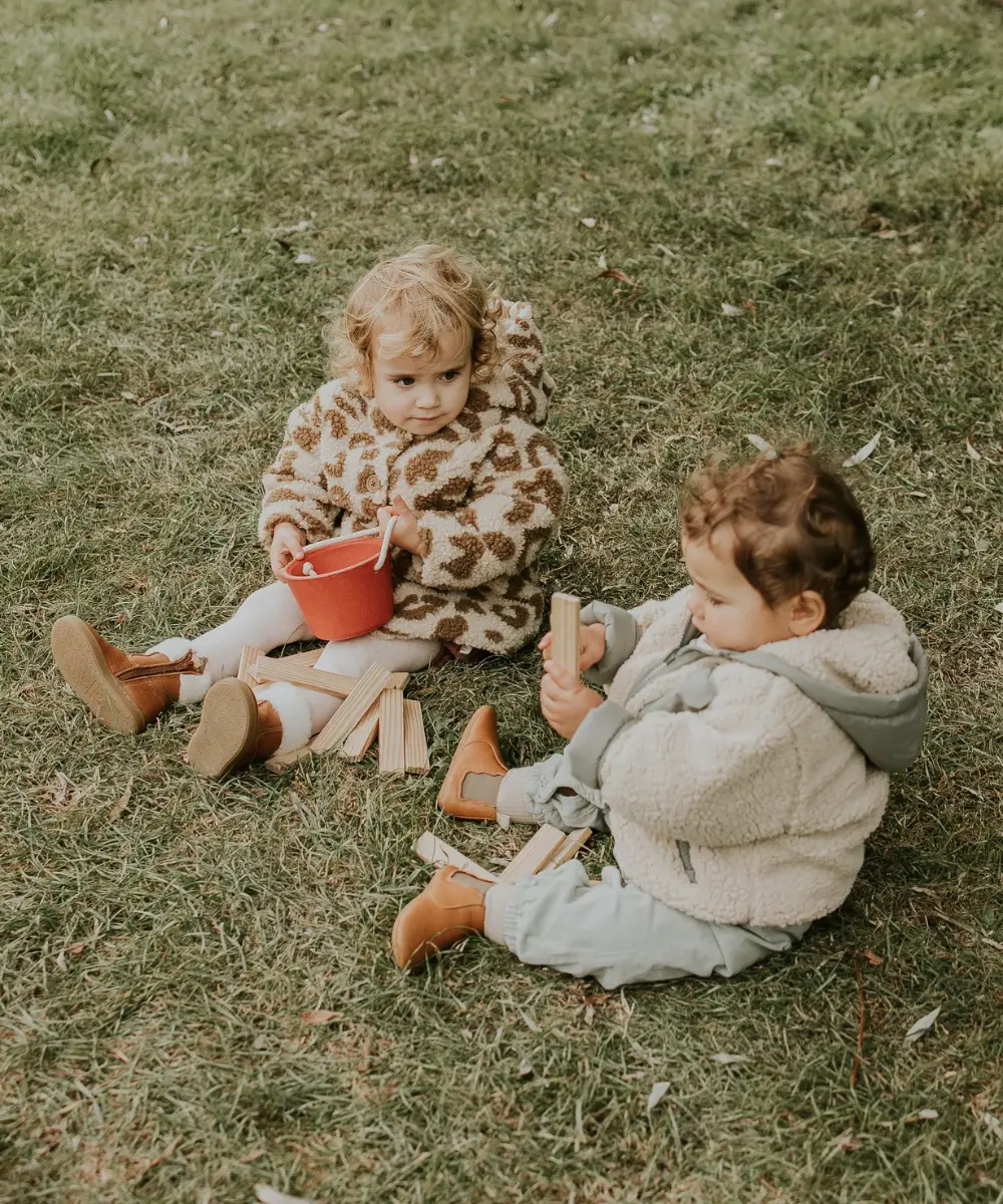 photo de deux enfants dans l'herbe portant des capucine marron et des oscars fourrés jouants à des jeux d'enfants