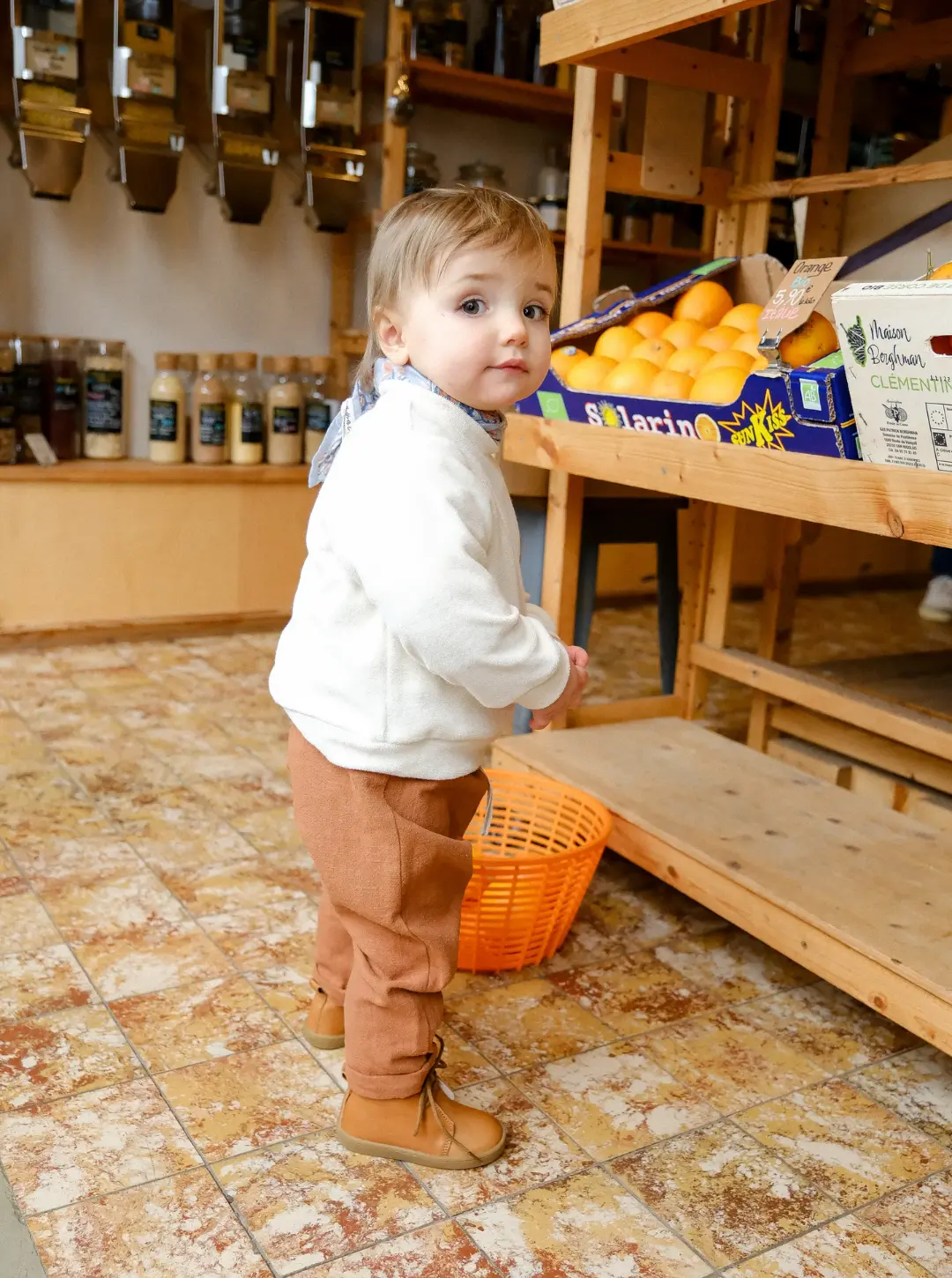 Enfant qui se tient debout dans une épicerie qui regarde vers la caméra en portant des raoul marron